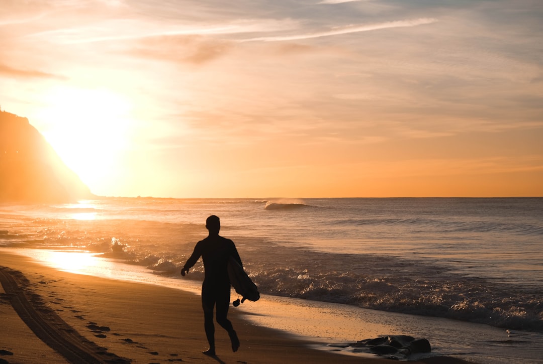 silhouette of man carrying surfboard running on shore,