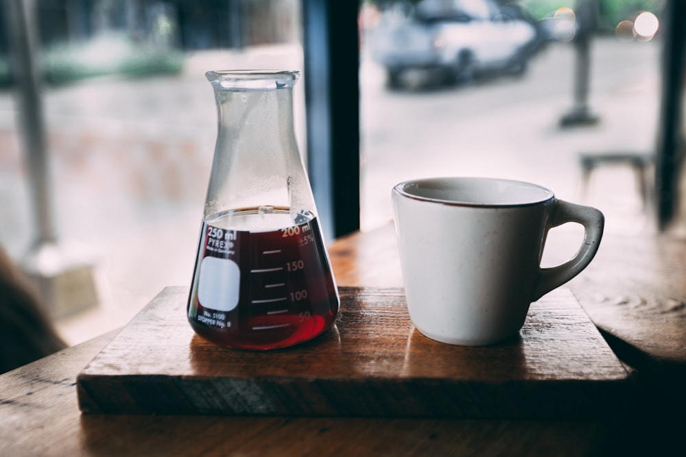 Frasco Erlenmeyer y taza de cerámica blanca sobre mesa de madera marrón