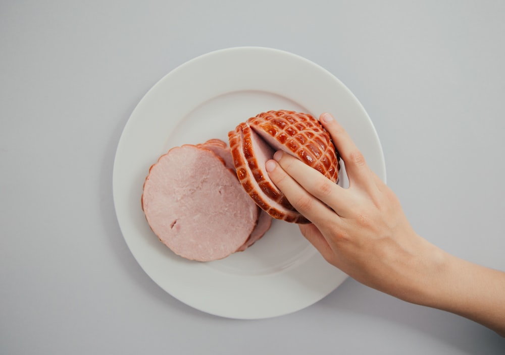 person holding sliced ham in white ceramic plate