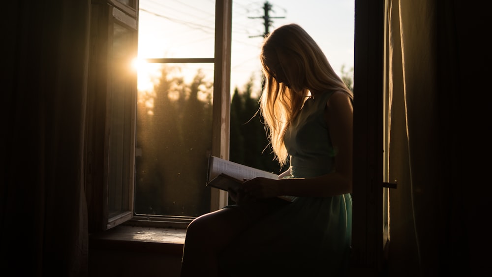 Frau liest Buch, während sie am Fenster sitzt