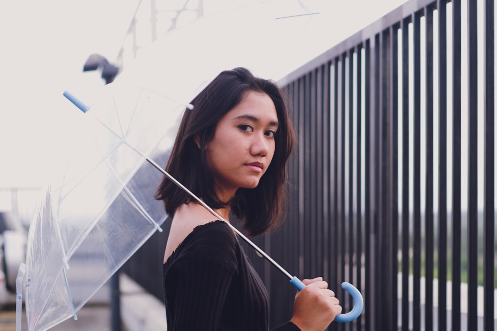 woman under open umbrella in front of black metal fence