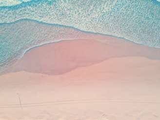 Aerial view of Prangtritis Beach with waves gently crashing on the shore under a soft pink sky.