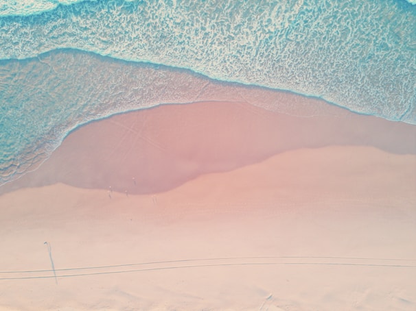 Aerial view of Prangtritis Beach with waves gently crashing on the shore under a soft pink sky.