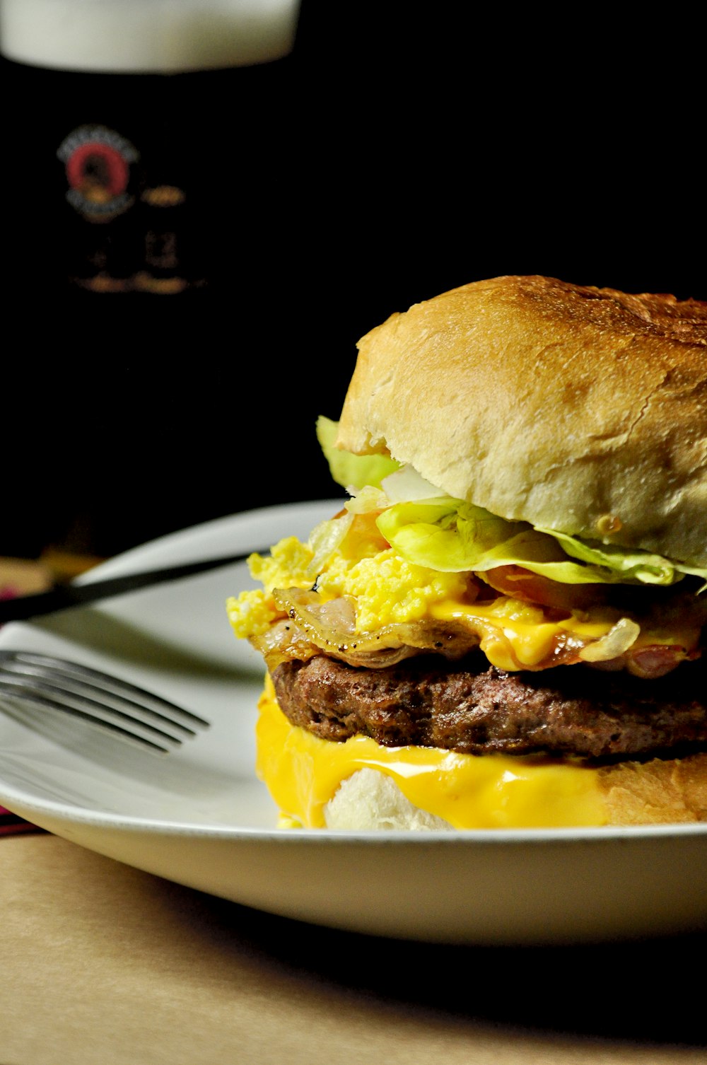 burger with cheese, lettuce and tomatoes on a white ceramic plate