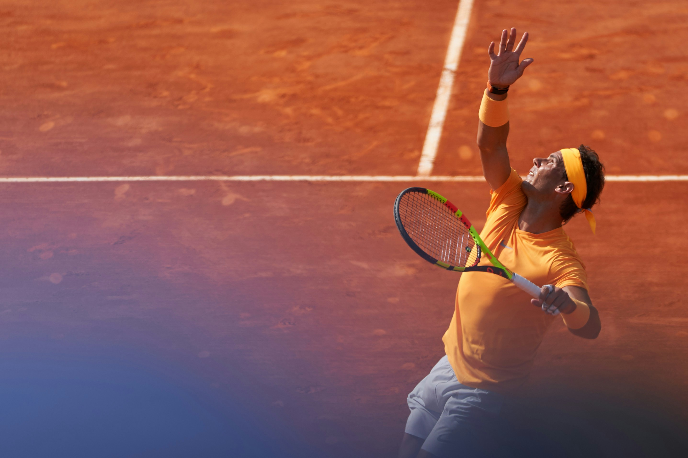 Tennis player mid-serve on a clay court, orange red surface, dramatic action shot, stadium crowd in background