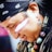 A person with long dark hair is wearing a black bandana with white patterns. They have face paint consisting of white and red stripes across the cheek. The person is adorned with colorful beaded jewelry around the neck and elaborate earrings with feather-like designs.