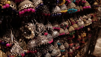 A collection of intricately designed earrings featuring traditional metalwork with colorful beads. The earrings are artistically arranged and illuminated, highlighting their detailed craftsmanship.