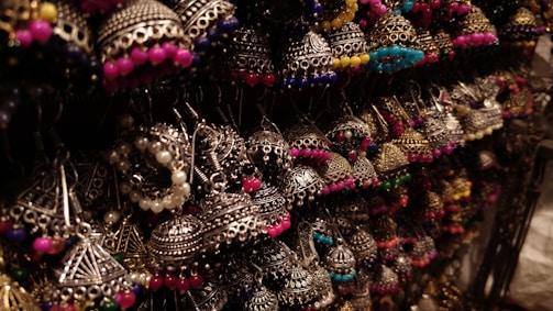 A collection of intricately designed earrings featuring traditional metalwork with colorful beads. The earrings are artistically arranged and illuminated, highlighting their detailed craftsmanship.