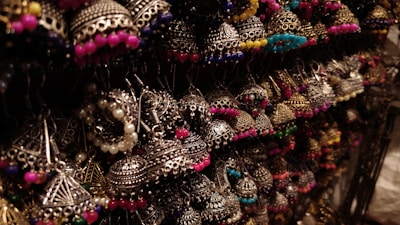 A collection of intricately designed earrings featuring traditional metalwork with colorful beads. The earrings are artistically arranged and illuminated, highlighting their detailed craftsmanship.