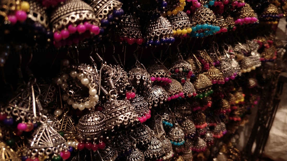 A collection of intricately designed earrings featuring traditional metalwork with colorful beads. The earrings are artistically arranged and illuminated, highlighting their detailed craftsmanship.