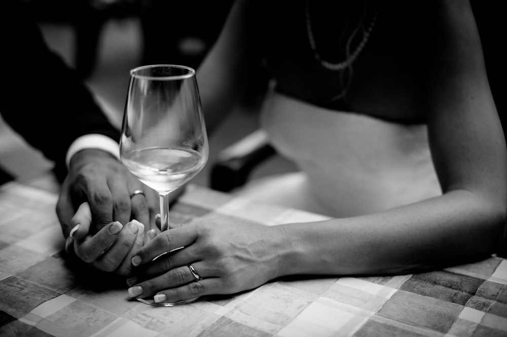 foto in scala di grigi di uomo che tiene la mano della donna che tiene il bicchiere di vino