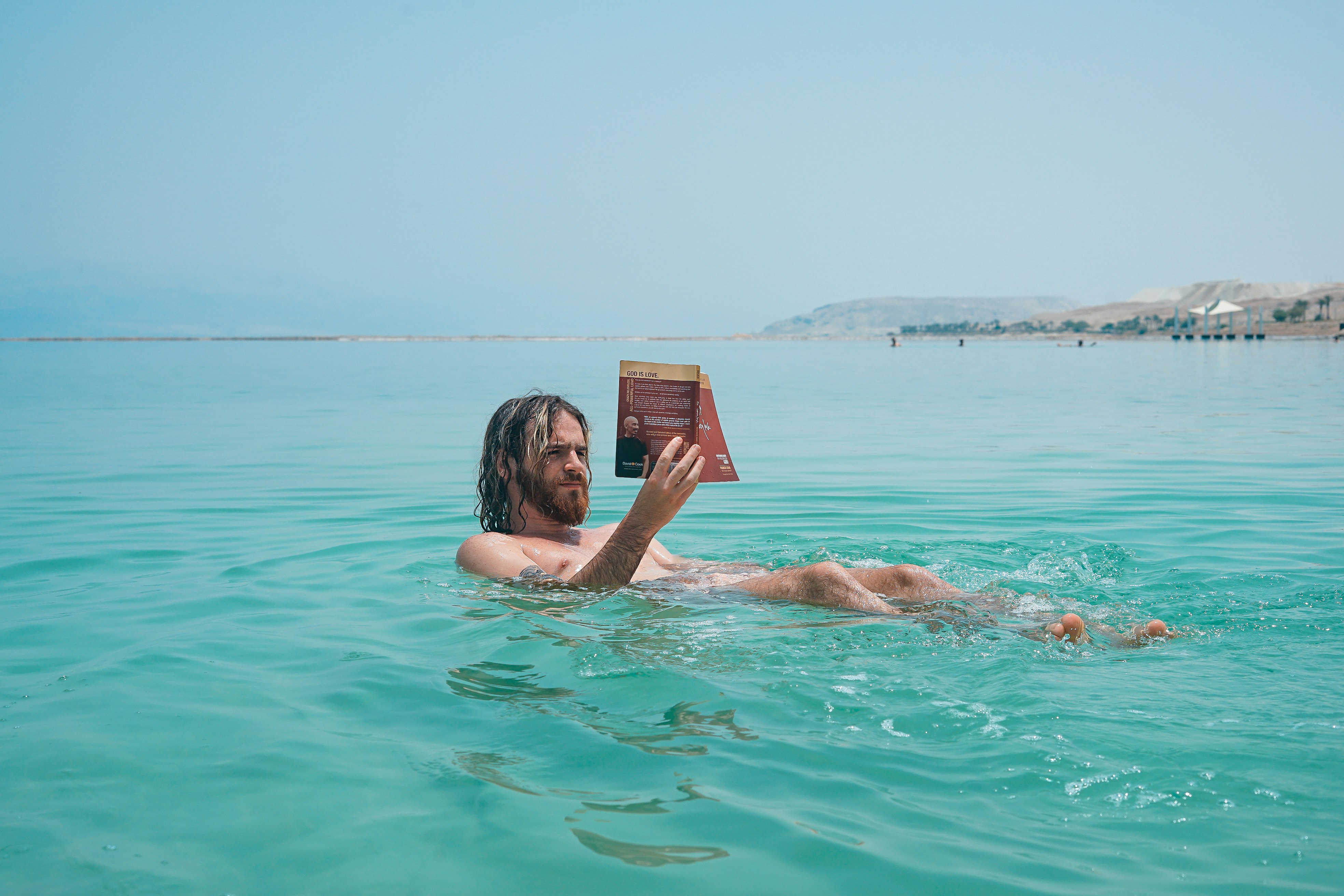 man floating on body of water while reading book