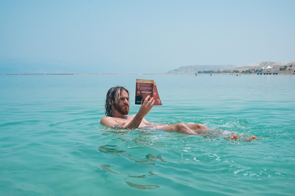 man floating on body of water while reading book