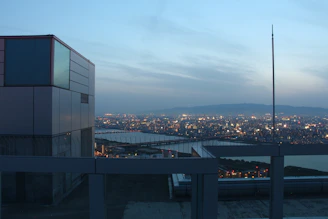 A panoramic view of a vibrant city skyline from a rooftop terrace, alive with evening energy.