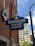 A blue sign with white lettering reads 'Ebenezer Baptist Church,' attached to the brick wall of a building. A cross is mounted on top of the sign. Below the sign is a vertical black pole, and in the background, there is a tall building with numerous windows. The sky is partly cloudy, and a white floral wreath is hung on the building.