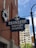 A blue sign with white lettering reads 'Ebenezer Baptist Church,' attached to the brick wall of a building. A cross is mounted on top of the sign. Below the sign is a vertical black pole, and in the background, there is a tall building with numerous windows. The sky is partly cloudy, and a white floral wreath is hung on the building.