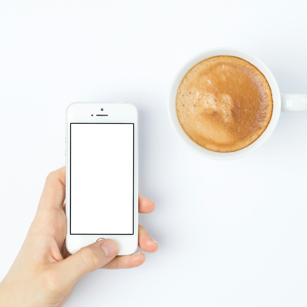 person silver iPhone 5s beside white ceramic mug