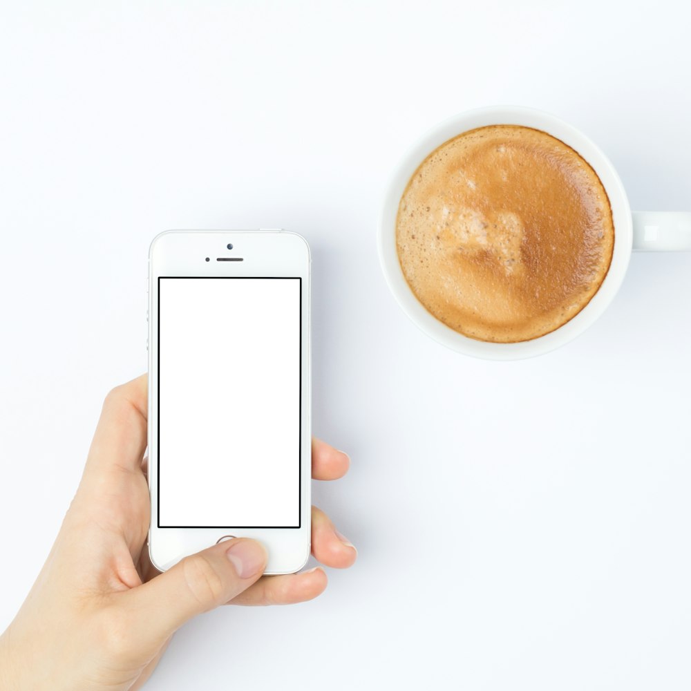 persona plateada iPhone 5s junto a taza de cerámica blanca
