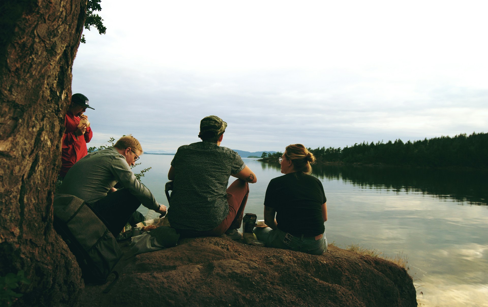 A group of friends enjoying a quilting session outdoors, with the river and mountains creating a picturesque backdrop.
