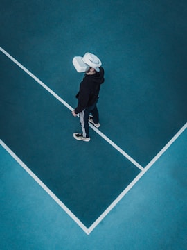 A person wearing a virtual reality headset stands on a large, empty sport court with distinct white lines on the floor. The dark clothing contrasts with the bright headset.