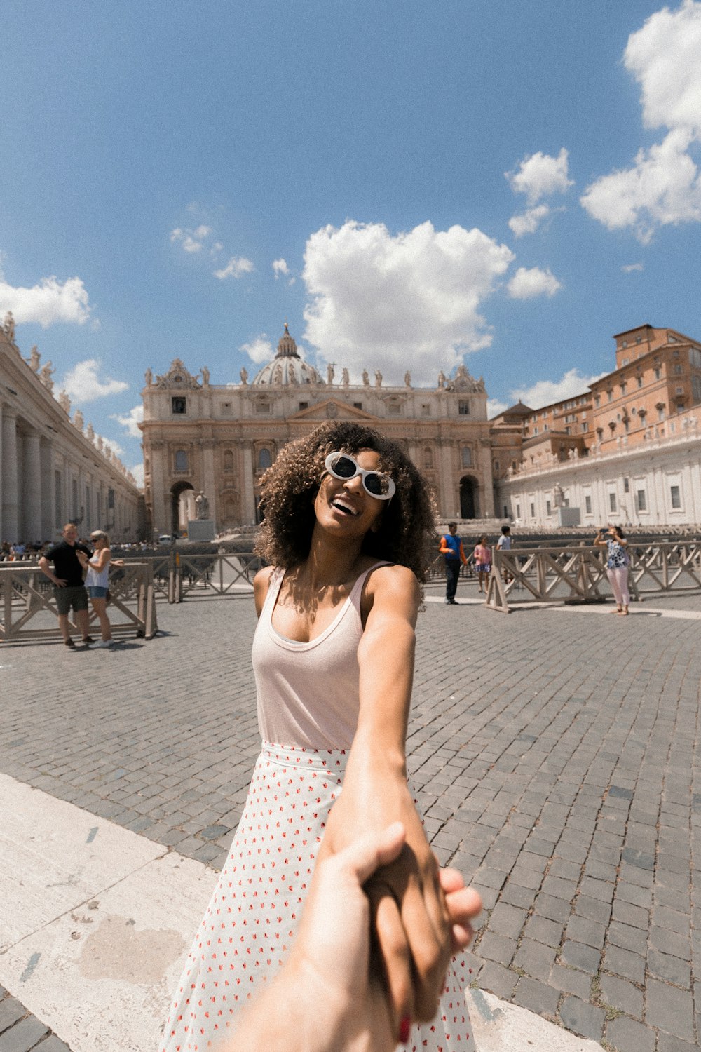 woman holding person's hand near buildings under white and blue cloudy sky