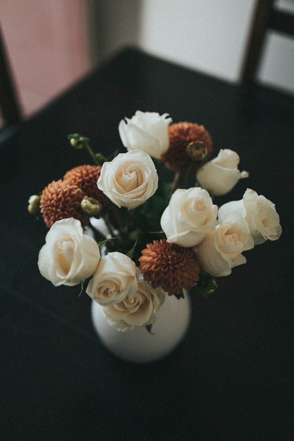 arranjo de flores brancas e alaranjadas em vaso de cerâmica branca sobre a mesa