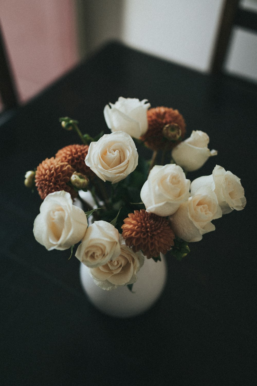 white and orange flower arrangement in white ceramic vase on table