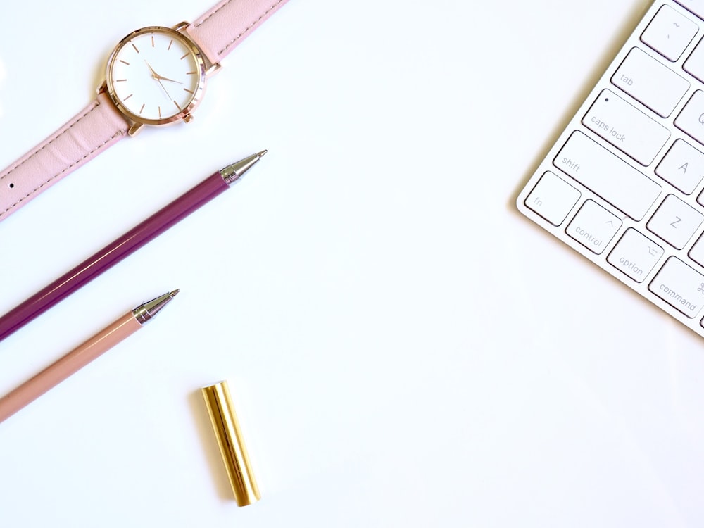 pink pen on table with round gold-colored analog watch