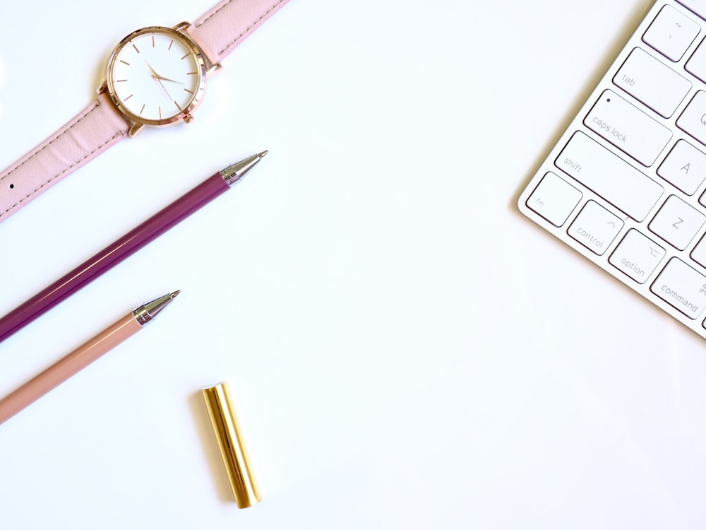 stylo rose sur table avec montre analogique ronde dorée