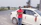 Man in casual clothes leaning on a car with countryside hills in the background.
