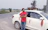 Man in casual clothes leaning on a car with countryside hills in the background.