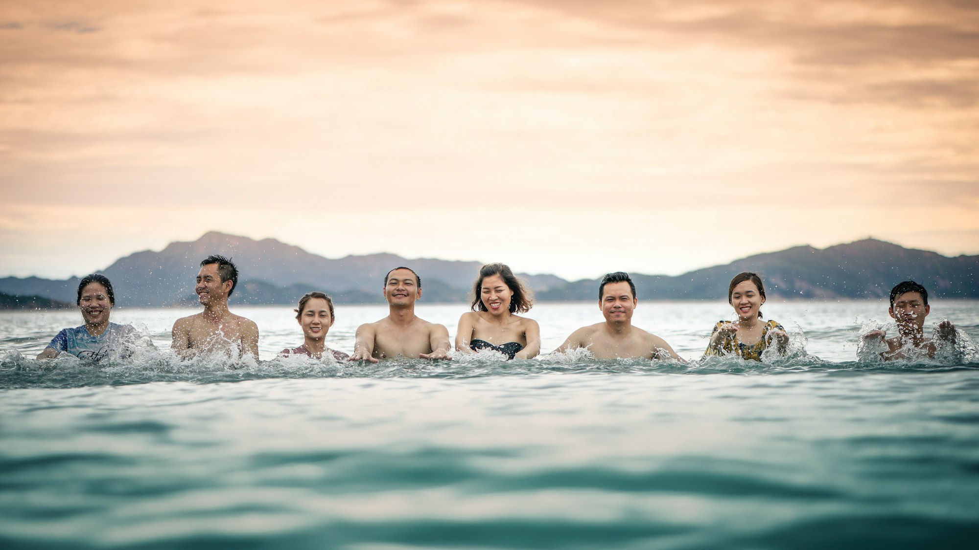 Seven people lined up, facing the camera, in the water. One of them has her eyes closed.