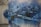 A large mural painted on a wall depicting an abstract aerial view of a cityscape. The artwork features a variety of buildings and streets, rendered in a blend of blues, blacks, and whites. There is a noticeable drip effect, creating a sense of movement or rain. A bridge with towers can be seen, adding to the urban landscape.