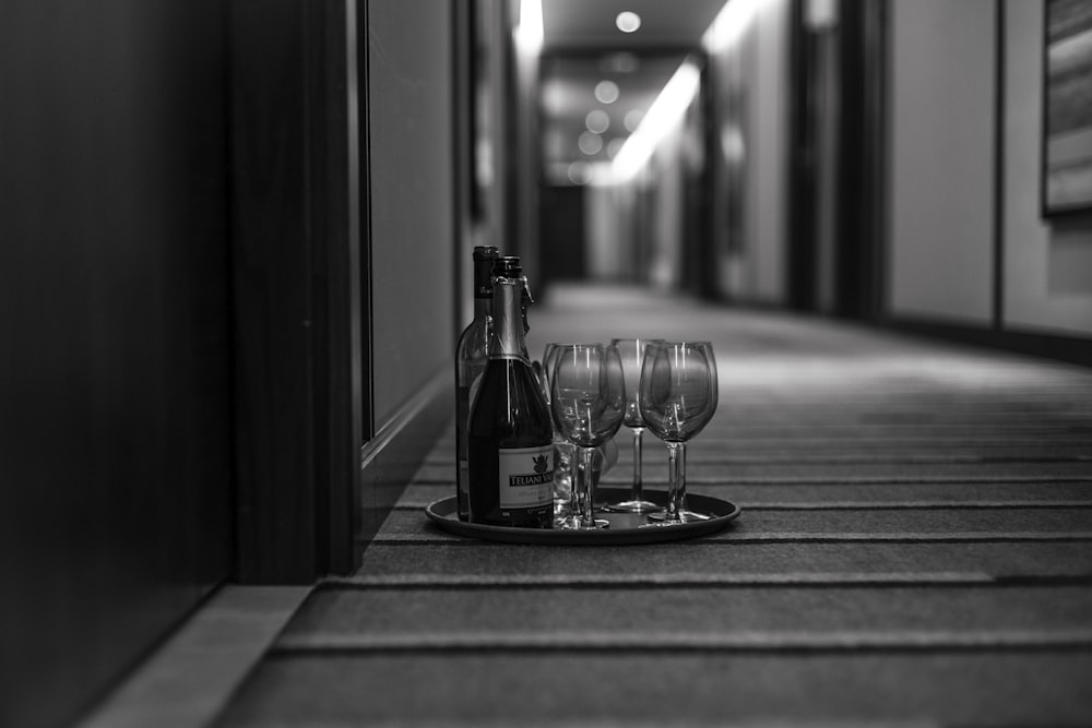 grayscale photo of wine glasses and bottle in tray