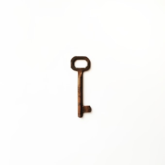 A rusty, old-fashioned key is placed against a plain white background. The key has an elongated shaft with a rectangular bow and a single toothed bit.