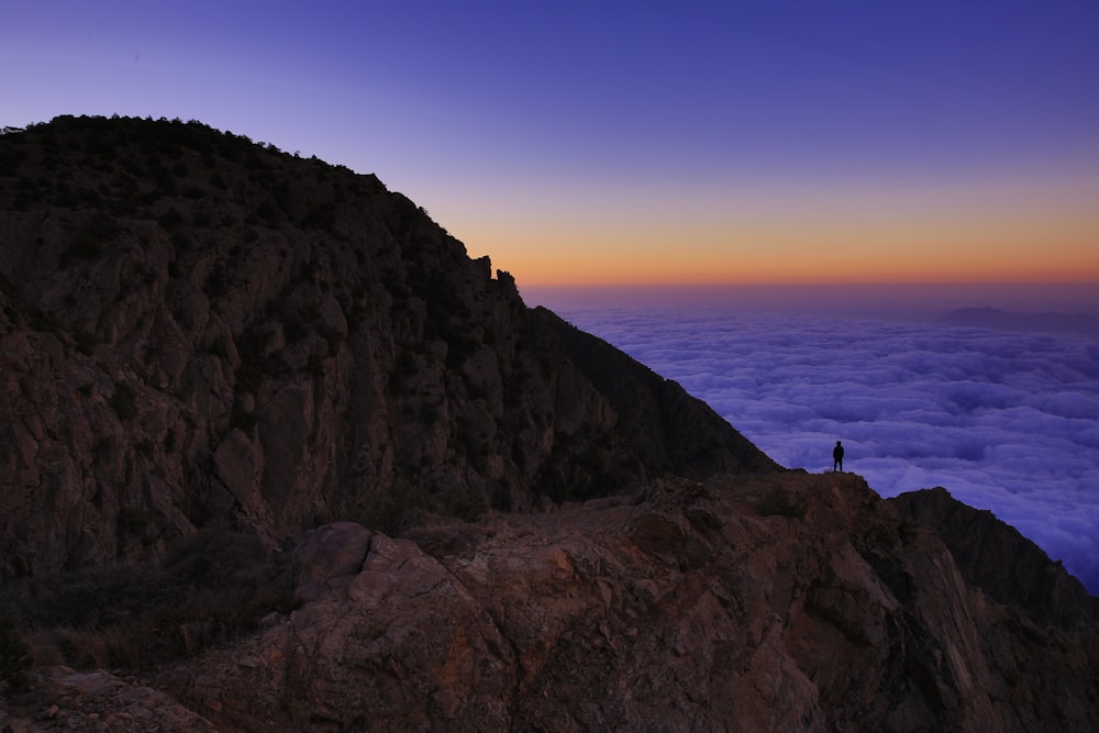 person standing on mountain in front of body of water