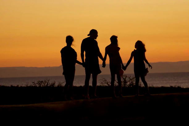 A family in silhouette holding hands against a warm orange sky by the sea