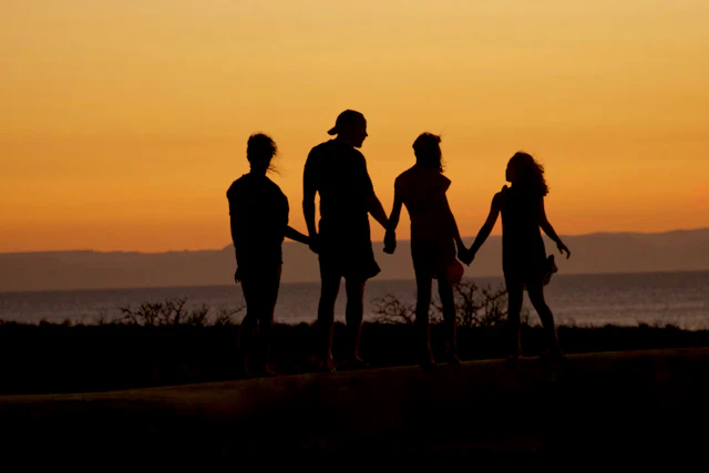 A family in silhouette holding hands on a beach at sunset