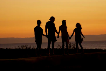 A family in silhouette holding hands against a warm orange sky by the sea