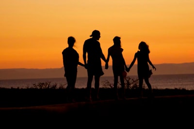 A family in silhouette holding hands against a warm orange sky by the sea