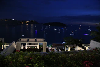 An evening scene of a yacht anchored near a quiet coastal village, lights glowing warmly onboard.