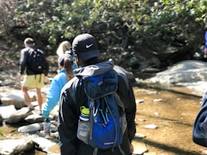 Backcountry hikers crossing a shallow stream, carrying backpacks and gear under a bright sky