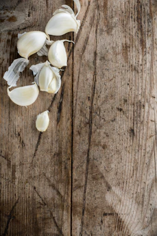 A heap of fine garlic powder with scattered garlic cloves on a wooden table.