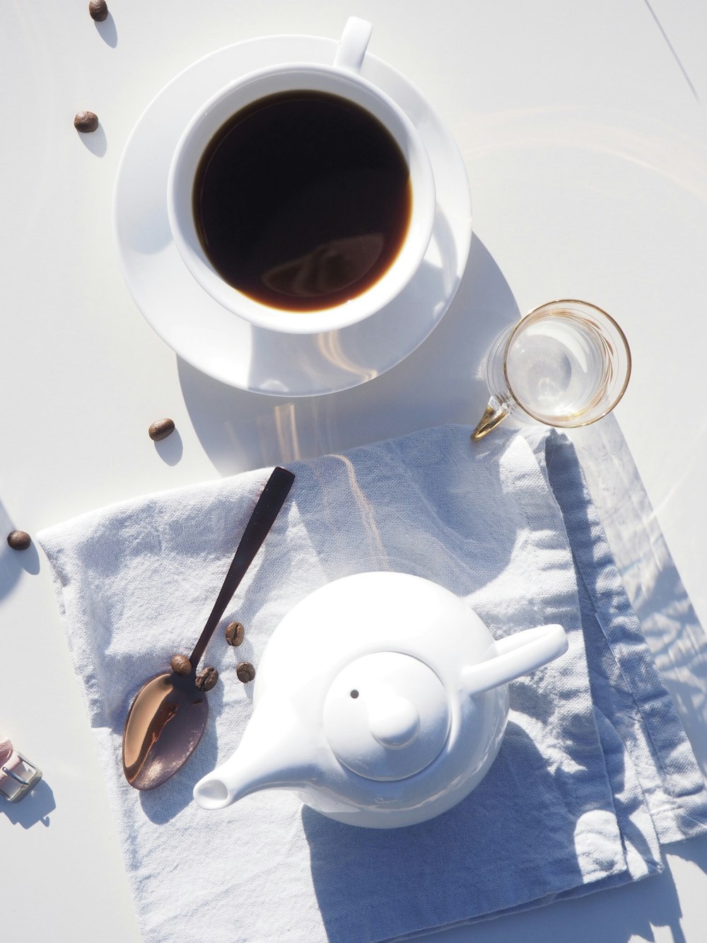 Tazza da tè in ceramica bianca riempita di caffè su piattino in ceramica bianca accanto a teiera in ceramica