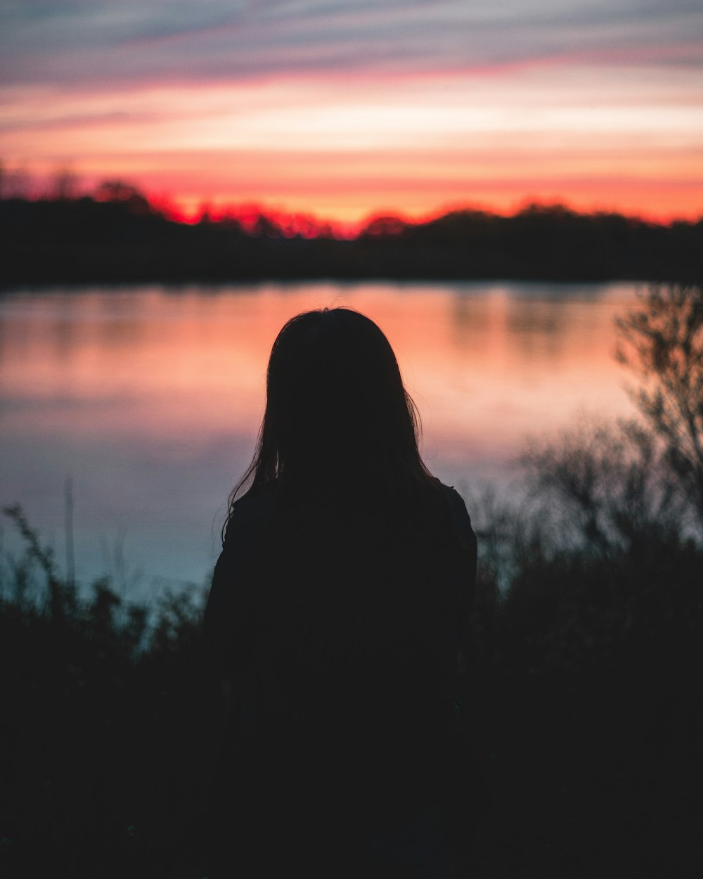 Frau blickt während des Sonnenuntergangs auf ein Gewässer