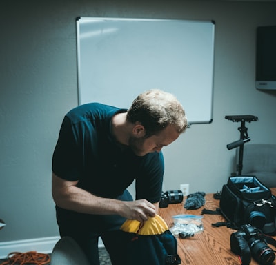 man holding blue and black bag near camera on desk