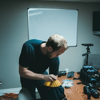 man holding blue and black bag near camera on desk