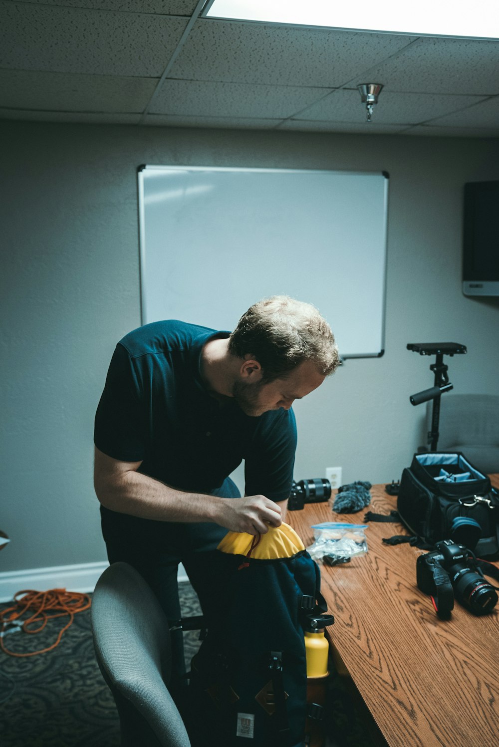 man holding blue and black bag near camera on desk