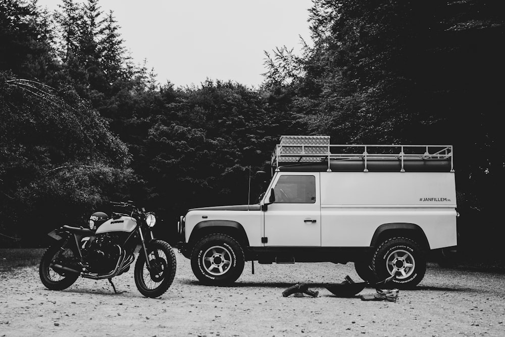 grayscale photography of motorcycle and car between trees