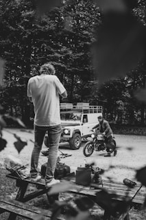 grayscale photography of man standing on picnic table